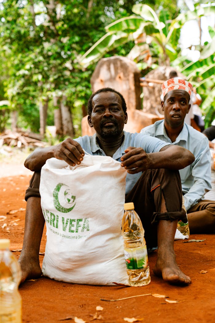 journey Two men sitting outdoors with food supplies, showcasing aid distribution.