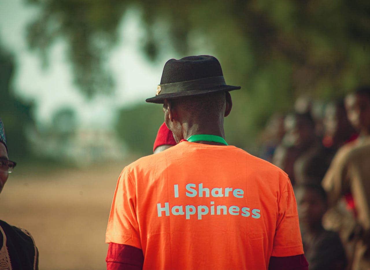 services-03 A man in an orange shirt with a happiness message stands outdoors, fostering positivity and community spirit.