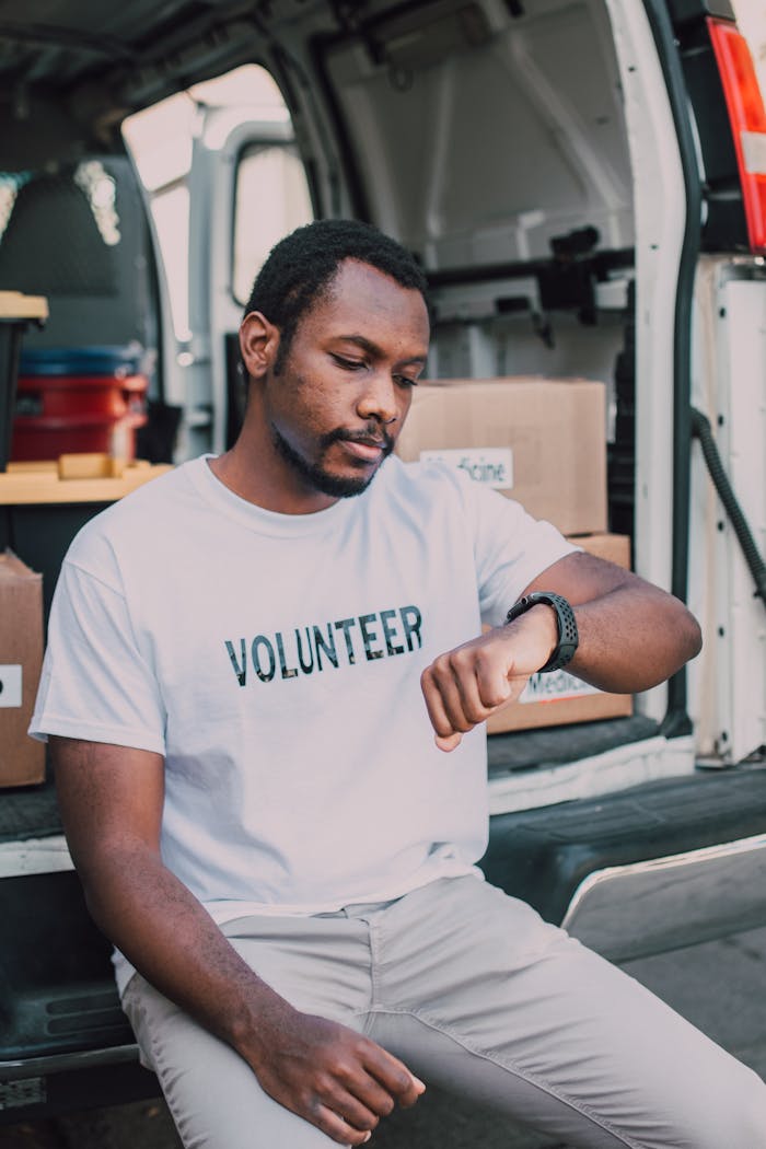 A volunteer sitting by a van, checking time, highlighting community service involvement.