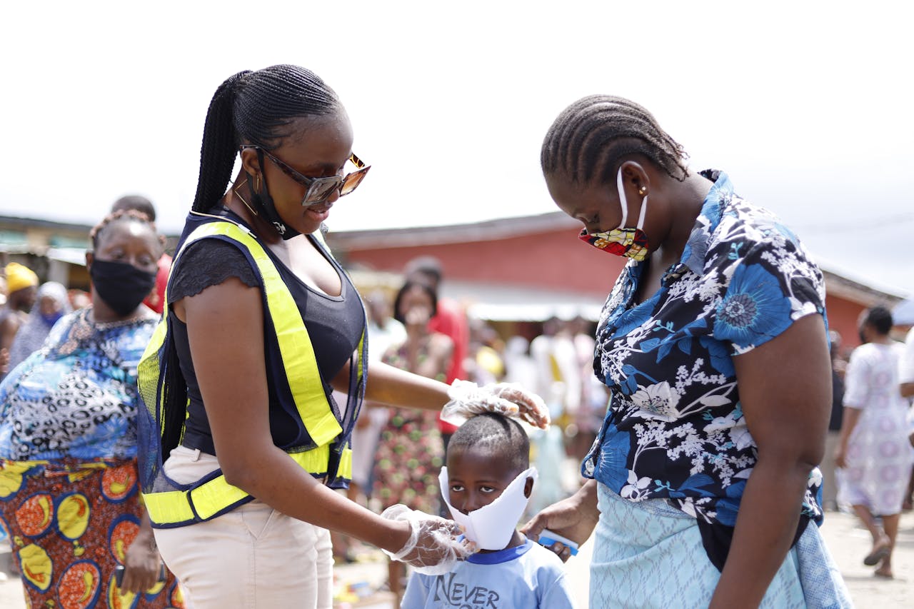 why-choose-us Women assisting a child with face mask in a community street setting.